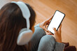 © oatawa - Woman with headphones holding mockup blank screen mobile smartphone while listening online music media entertainment relaxation on sofa at home, White empty space for advertise text.
