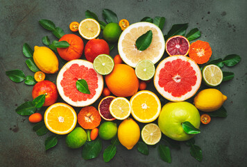 Wall Mural - Colorful citrus fruis, food background, top view. Mix of different whole and sliced fruits: orange, grapefruit, lemon, lime and other with leaves on  green stone table