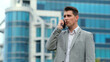 © wedmoments.stock - Close-up of a man talking on a mobile phone near an office building. Close-up of a businessman talking on the phone on the street in slow motion. Portrait of a happy business man calling on the phone.