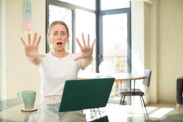 Poster - caucasian pretty woman with a laptop feeling stupefied and scared, fearing something frightening, with hands open up front saying stay away