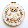 A cute teddy bear wearing a cream dress embroidered on a circular embroidery frame, isolated against a white background - gift for a child at a baby shower - Generative AI