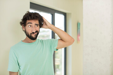 Wall Mural - young crazy bearded man feeling puzzled and confused, scratching head and looking to the side
