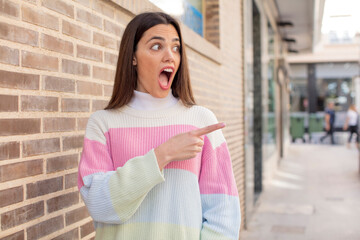 Wall Mural - pretty young adult woman feeling joyful and surprised, smiling with a shocked expression and pointing to the side