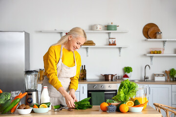 Poster - Mature woman with fresh vegetables and fruits making healthy smoothie in kitchen