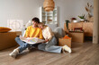 © Pixel-Shot - Young couple with house plan sitting in room on moving day