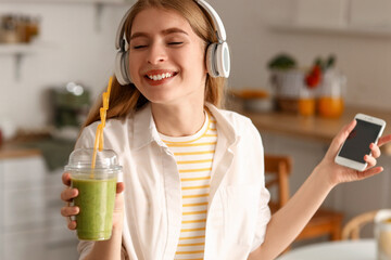 Wall Mural - Young woman in headphones with glass of healthy smoothie and mobile phone at home, closeup