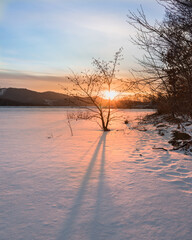 Wall Mural - Winter landscape. Sunset over a frozen lake that is covered in snow.