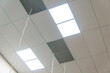 White suspended ceiling with square fluorescent lights in an office space. Design and details of a modern ceiling and lighting devices. Details of the modern interior.