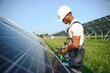 African american man in safety helmet and glasses tighten nuts on solar panels with screwdriver. Competent technician using tools while performing service work on station