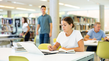 Wall Mural - Portrait of young woman studying at library using books and laptop