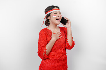 Happy mindful thankful young Asian woman wearing red kebaya and holding phone and hand on chest smiling isolated on white background feeling no stress,