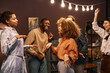 © Seventyfour - Group of young intercultural excited friends dancing together at home party while standing in front of camera in living room