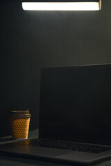Black laptop screen and a cup of coffee in a dark room.