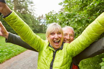 Wall Mural - Happy elderly couple wearing jackets hiking in forest