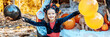 little girl in spooky cute costume and hat stands near trunk car decorated for Halloween with web, orange balloons and pumpkins, outdoor creative activity concept in autumn