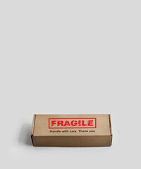 A rectangular cardboard box. Monochrome light background. An adhesive warning labels for packaging - Fragile, Handle with care, Thank you. Red, black, white, beige colors. Textured font design