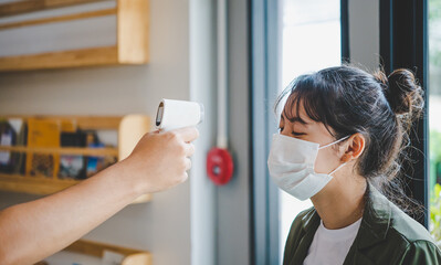 Hand holding infrared thermometer to measuring temperature  people with face mask on background. Covid flu screening 19 concept.