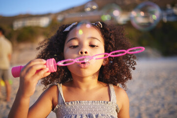 Wall Mural - Girl child, beach and blowing bubbles with playing, outdoor and freedom on sand, games and thinking in nature. Female kid, soap and water with plastic toys with wind, summer sunshine and vacation