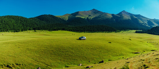 Wall Mural - Modern car on a green hill in a picturesque mountains valley panorama, travel concept