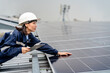 © sirichai - Woman engineer electrician using a hand to check solar panels on the roof, clean energy power nature, photovoltaic systems, the energy produced by the sun, sustainable business concept.
