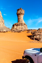 World Cup Naturally Shaped Stone Rock And 4x4 Vehicle Front Part. Sahara Desert Of Tadrart Rouge, Djanet, Algeria. Offroad Car Looking At Rocky Mountains And A Rock With The Shape Of A Rook. Blue Sky.
