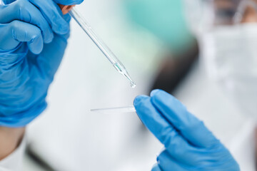 Wall Mural - Scientist analyzing microscope slide at laboratory. Young woman technician is examining a histological sample, a biopsy in the laboratory of cancer research, Hand in blue glove holding glass histology