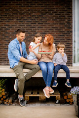 Wall Mural - Family with a mother, father, son and daughter sitting outside on steps of a front porch of a brick house and eating strawberries