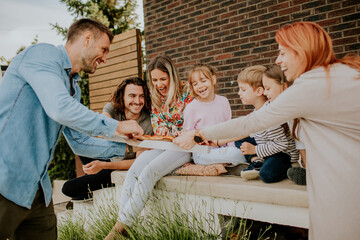 Group of young people and kids eating pizza in the house backyard