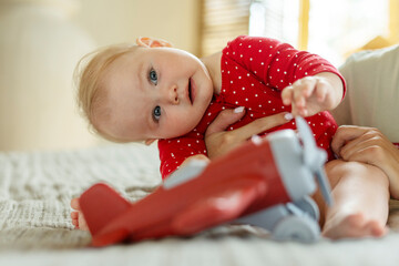 Wall Mural - Portrait of smiling baby sitting on bed in living room at home, playing with airplane