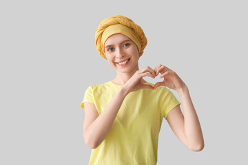 Sticker - Teenage girl after chemotherapy making heart with her hands on light background