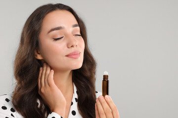 Poster - Beautiful young woman with roller bottle of essential oil on light grey background, space for text