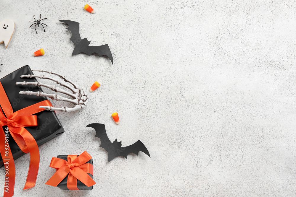 Composition with gift boxes, tasty candy corns, skeleton hand and Halloween decor on light background