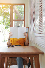 Woman Covering Her Face With Blank Book Or Magazine At Home.
