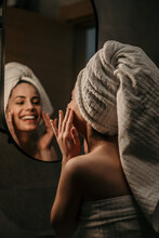 Smiling Woman Applying Some Creme On Her Face Skin In Front Of The Mirror.