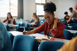 © Drazen - Black female student takes notes while learning during class at lecture hall.