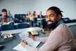 © Drazen - Happy black teacher reviewing test of adult students during education exam in lecture hall and looking at camera.