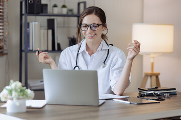 female doctor with laptop consulting patient online by computer video call conversation in her hospital office, Healthcare and medical concept.