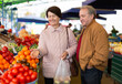 Elderly man and a woman buy fresh tomatoes at an indoor market