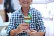 © luciano - Smiling senior woman sitting at cafe table holding a glass with specialty of Canary island called barraquito, made with condensed milk, coffee and liqueur