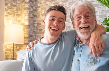 Wall Mural - Portrait of family couple, a young boy and his old grandfather smiling looking at camera while sitting on the sofa at home, old and new generation - caring for the people we love