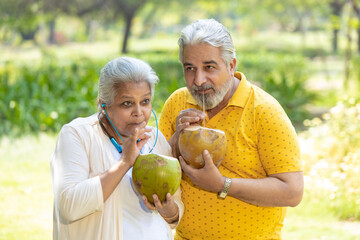 Indian senior couple drinking coconut water at park.