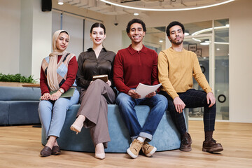 Wall Mural - Full length portrait of young Middle Eastern business team posing together in modern office all looking at camera cheerfully