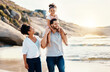 © Ramba/peopleimages.com - Family on beach, kid on father shoulders and travel with bonding, love and walking together in nature. Vacation, ocean and happy people outdoor, parents and kid with sunshine and adventure with fun