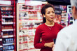 A pretty African woman talking with a male pharmacist next to a makeup shelf.