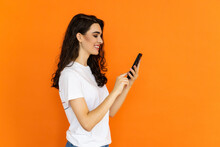 Young Girl Looking Confused At Her Phone Over Orange Background.