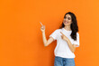 Beautiful girl pointing to the side on orange background