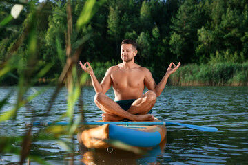 Wall Mural - Man meditating on color SUP board on river