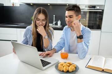 Wall Mural - Female and male teenagers using laptop together and eating croissants .