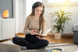 © Bojan - Focused teenage girl student with headphones taking notes to notebook while listening online audio course and sitting on floor at home.