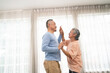 © artitwpd - Romantic and cheerful Asian well-being senior couple enjoy dancing and holding hands to music together with smiles and happiness in the living room. Senior retirement activity at home.
